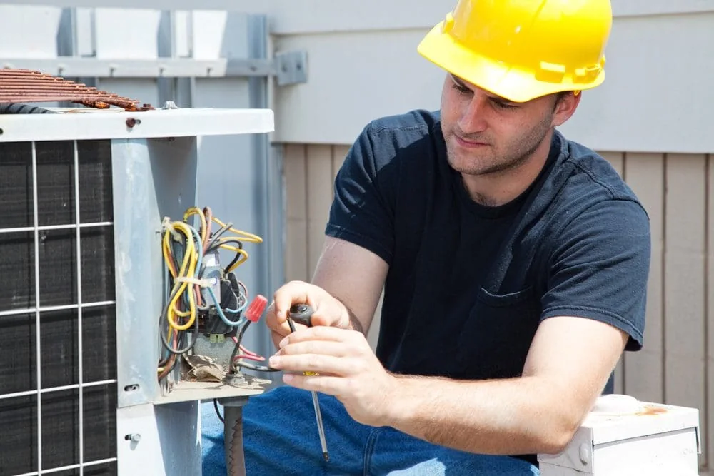 HVAC technician repairing the electrical components of an outdoor air conditioning unit