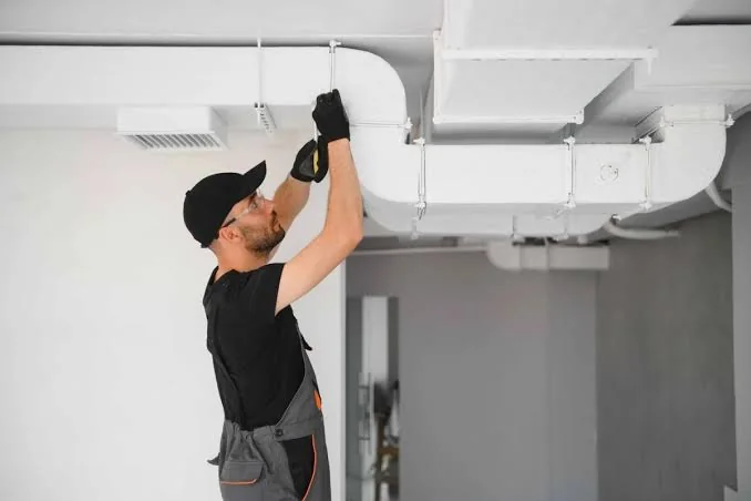 HVAC technician inspecting overhead ductwork and airflow components