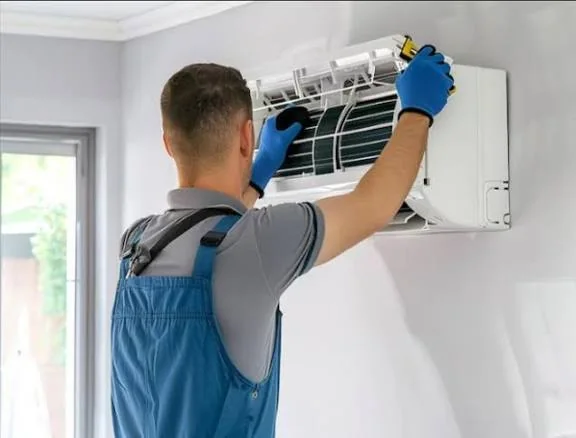 Technician servicing the air filter inside a wall-mounted HVAC unit
